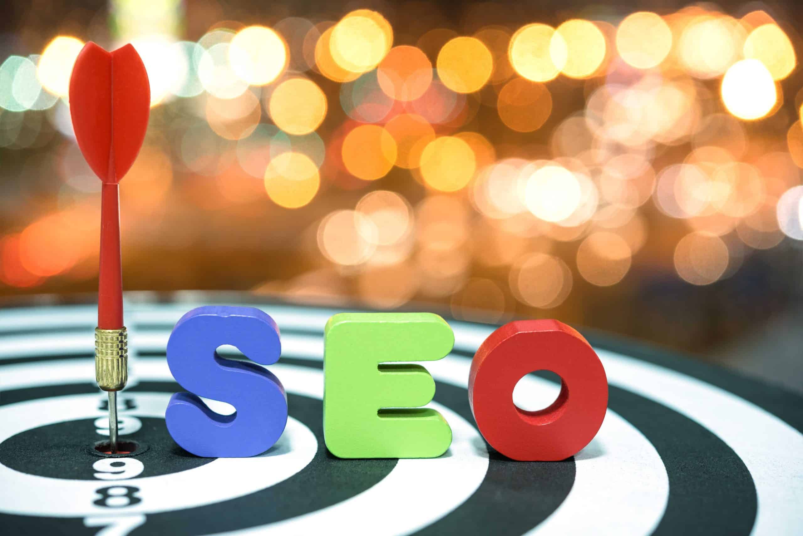 A red dart hits the center of a black and white target, with colorful "SEO" letters in the foreground symbolizing White Label SEO Services for Agencies, set against a backdrop of blurred lights.
